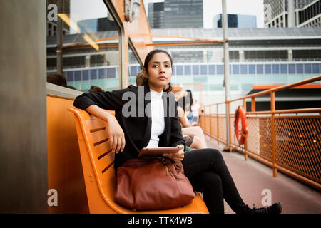 Thoughtful woman using digital tablet while sitting on bench in city Stock Photo