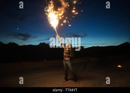 Woman burning fireworks on mountain against sky at dusk Stock Photo