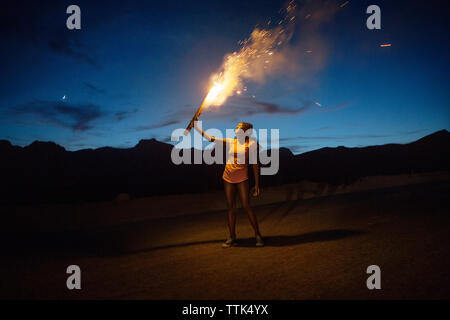 Smiling woman burning fireworks on mountain against sky at dusk Stock Photo