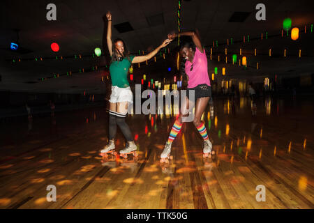 Friends dancing while roller skating at illuminated roller rink Stock Photo