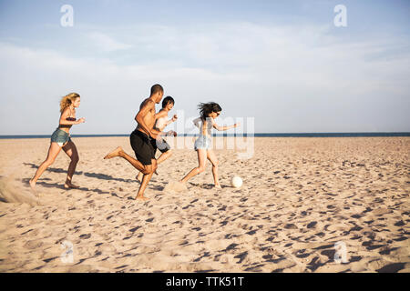 Friends playing soccer on sand at beach against sky Stock Photo