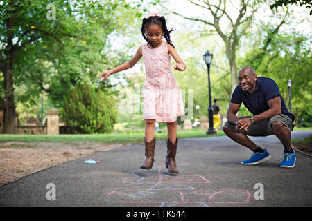 Father and daughter playing hopscotch on road at park Stock Photo