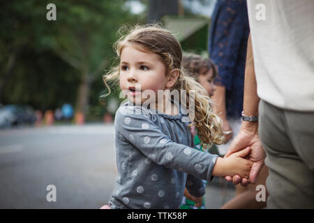 Girl looking away while holding father's hand on street Stock Photo