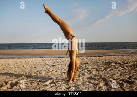 Side view of woman doing handstand at beach against sky Stock Photo