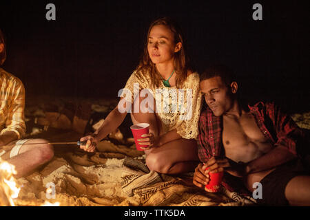Couple sitting by bonfire at beach Stock Photo