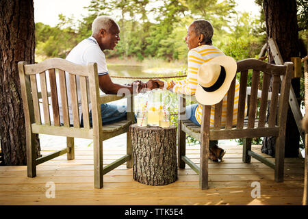 Senior couple holding hands while sitting on chairs by lake Stock Photo
