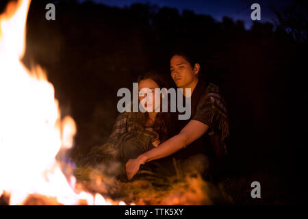 Couple wrapped in blanket sitting by campfire at night Stock Photo