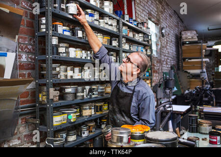 Man picking up ink container from shelves at letterpress workshop Stock Photo