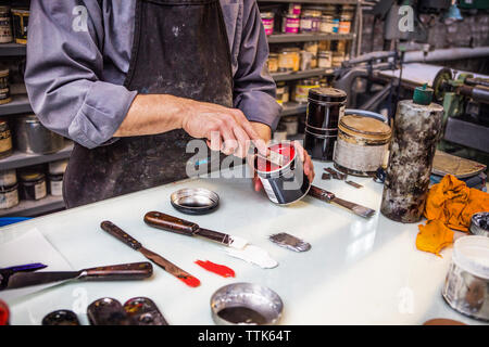Midsection of man removing paint from can with ink knife on table Stock Photo