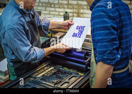 Midsection of coworkers examining paper while standing by machinery in workshop Stock Photo