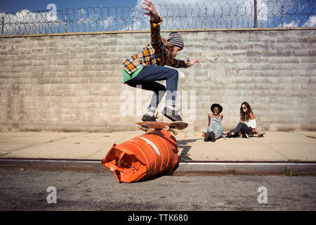 Young man performing skateboard stunt over barrel on street Stock Photo