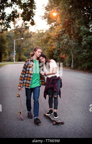 Woman resting head on man's shoulder while standing on skateboard Stock Photo