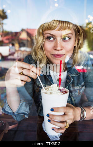 Thoughtful woman looking away while holding milkshake glass in cafe Stock Photo