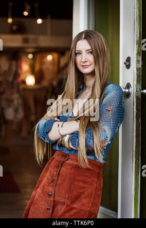 Portrait of woman with arm crossed leaning on boutique entrance Stock Photo