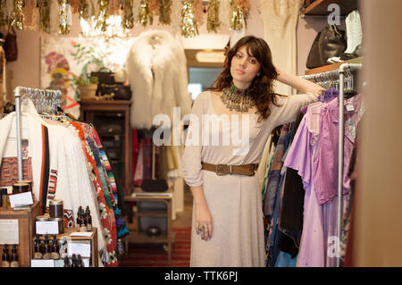 Portrait of woman leaning on clothes rack at boutique Stock Photo