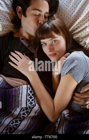 Man kissing woman on forehead while lying on bed in camper van Stock Photo