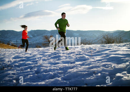 Couple jogging on snow field against sky Stock Photo