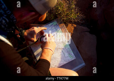 Overhead view of man using navigational compass on map while sitting on field Stock Photo