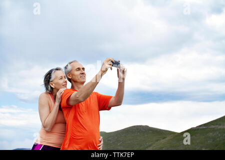 Couple photographing with smart phone against cloudy sky Stock Photo