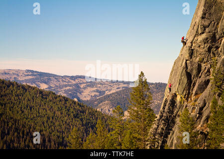 Climbers climbing mountain by forest against clear sky Stock Photo