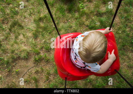 Overhead view of baby boy swinging on red plastic swing at playground Stock Photo
