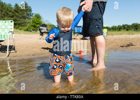 Low section of father holding cute son's hand while standing in lake against clear sky Stock Photo