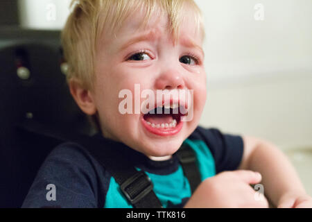 Close-up portrait of angry baby boy crying while sitting on high chair at home Stock Photo