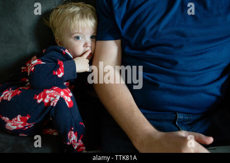 Toddler boy makes hand gesture to be quiet while sitting next to father on couch Stock Photo