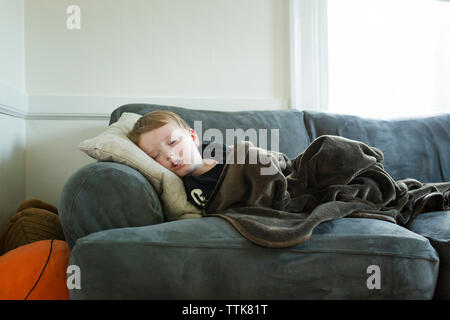 Preschool age boy naps on couch covered with a blanket Stock Photo
