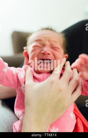 Newborn baby girl in pink pajamas held upright cries in mother's hands Stock Photo