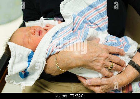 Grandmother holds newborn baby wrapped in blanket in hospital room Stock Photo