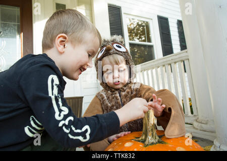 Two male children dressed for Halloween touch pumpkin on front porch Stock Photo