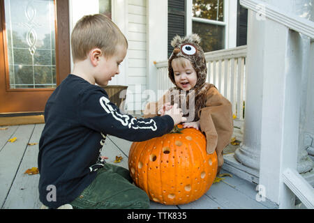 Two boys play with jack o lantern on front porch while dressed up Stock Photo