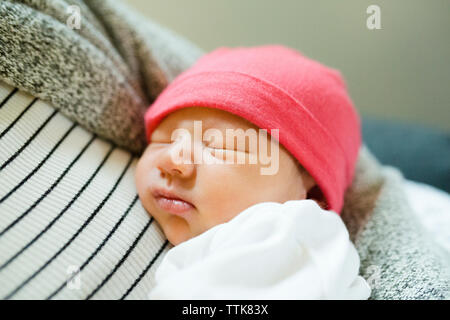 Sleeping newborn baby girl being held in mother's arms wearing hat Stock Photo