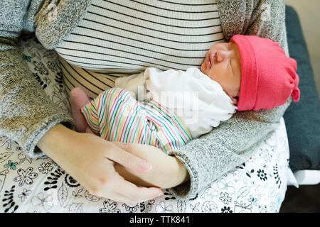 Mother holding newborn daughter in her arms while sitting in chair Stock Photo