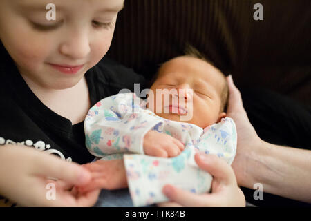 Newborn baby girl being held by elementary age boy on couch Stock Photo
