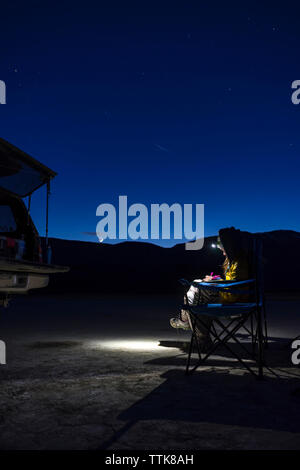 Female hiker using headlamp at night while sitting on camping chair Stock Photo