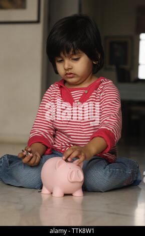 Indian girl putting a coin into a piggy bank Stock Photo - Alamy