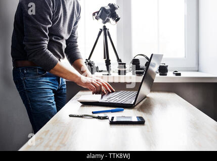 Midsection of man using laptop on table against window Stock Photo