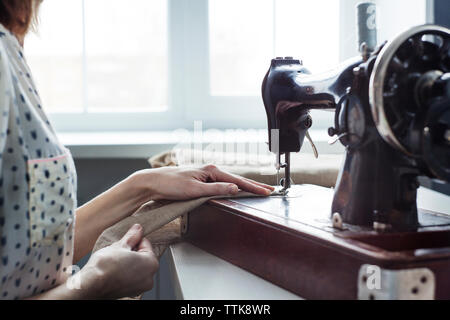 Midsection of woman using sewing machine on table against window Stock Photo