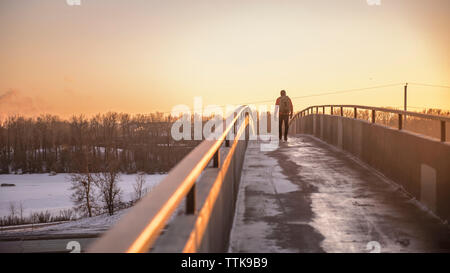 Man walking toward the sun at sunset on footbridge with backpack Stock Photo
