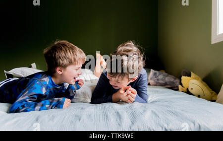 Happy brothers talking while lying on bed at home Stock Photo