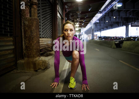 Front view of woman in starting position ready to run by bridge Stock Photo