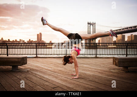 Woman doing splits on handstand at promenade against Manhattan bridge Stock Photo