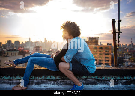 Couple embracing on rooftop against sky during sunset Stock Photo