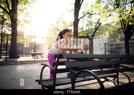 Woman stretching on wooden bench at park Stock Photo