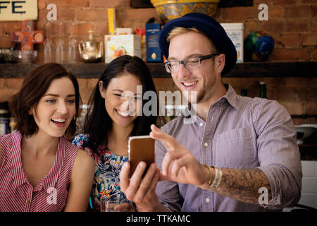 Man showing phone to female friends while standing at kitchen counter Stock Photo