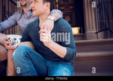 Midsection of gay couple sitting on steps outside house Stock Photo