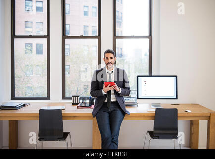 Portrait of businessman using tablet computer while leaning on desk in office Stock Photo