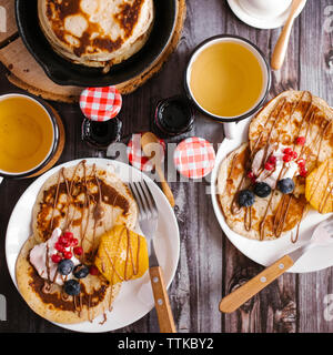 Overhead view of pancakes with preserves and fruits on wooden table Stock Photo